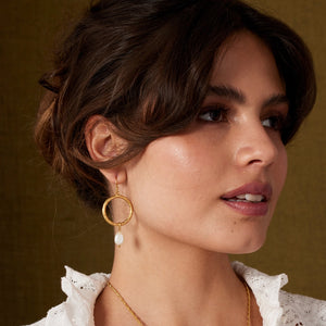 Close-up of a woman wearing gold hoop earrings with a brown background