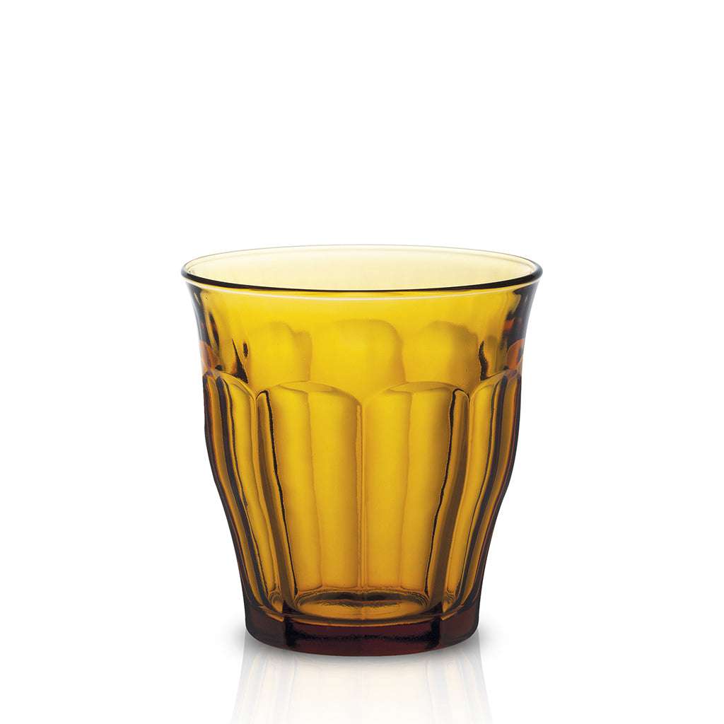 Amber-colored glass with a drink and ice cubes on a wooden surface with a plant in the background