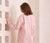 Woman wearing a pink and white striped shirt against a white wall.