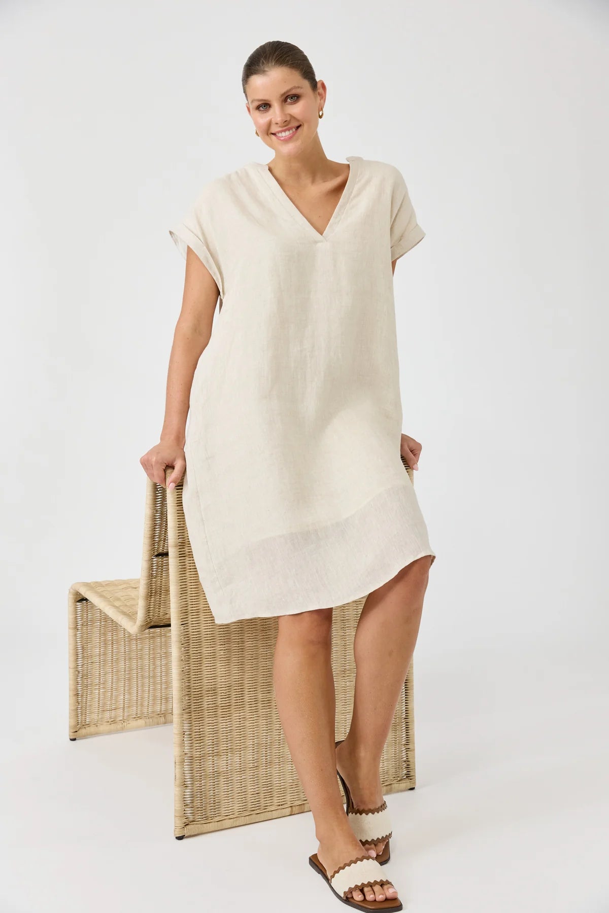 Woman wearing a beige dress holding a woven bag on a white background