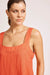 Woman wearing an orange sleeveless top against a plain background