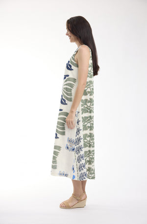 A woman modeling a sleeveless midi dress with a green and blue botanical leaf pattern on a white background, shown from a side profile against a plain white studio backdrop.
