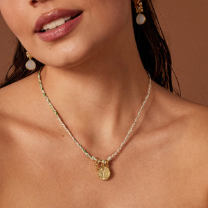 Close-up of a woman wearing a green plaited necklace with a pendant on a brown background