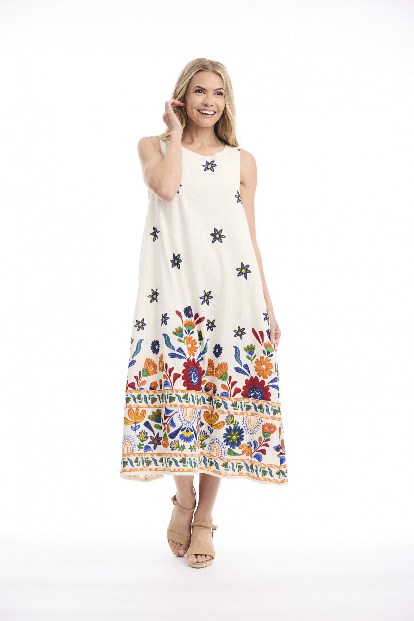 A woman modeling a sleeveless cream maxi dress with colorful floral embroidery and star motifs, set against a plain white studio background.