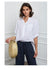 Woman wearing a white shirt and  pants holding a straw bag against a white wall.