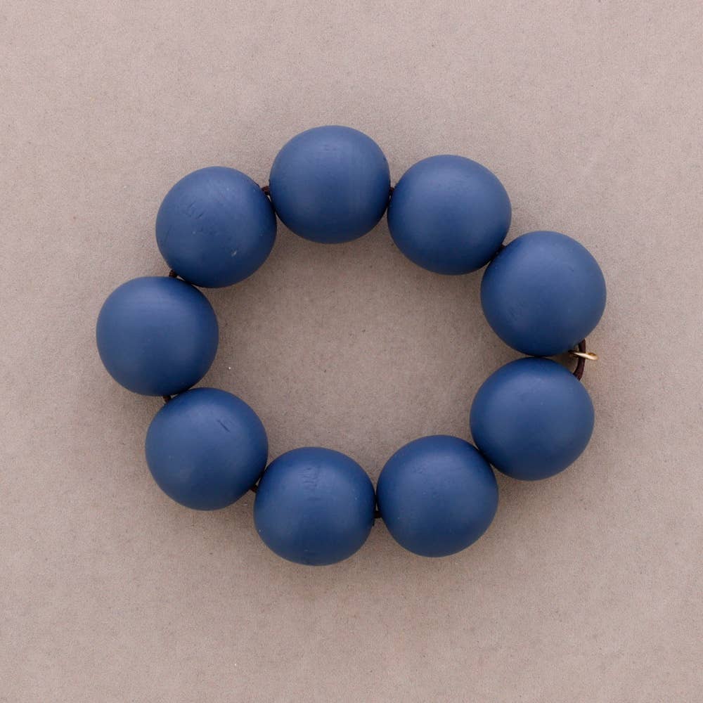A beaded bracelet made of matte, dark red-brown round beads arranged in a circle on a neutral beige background.