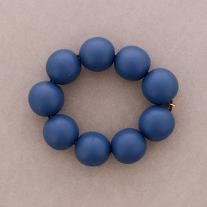 A beaded bracelet made of eight matte blue round beads, arranged in a circle on a neutral taupe background.