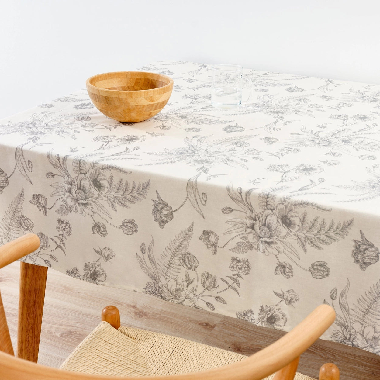Floral-patterned tablecloth on a wooden table with a bowl and chair.