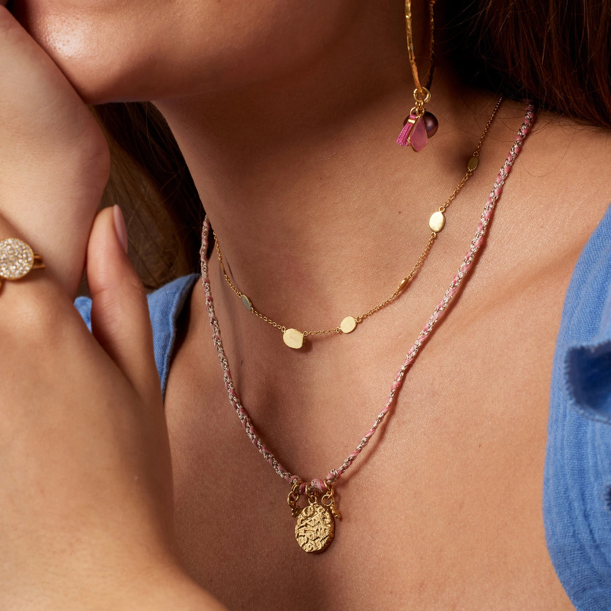 Necklace with gold charm and pink thread on a white background