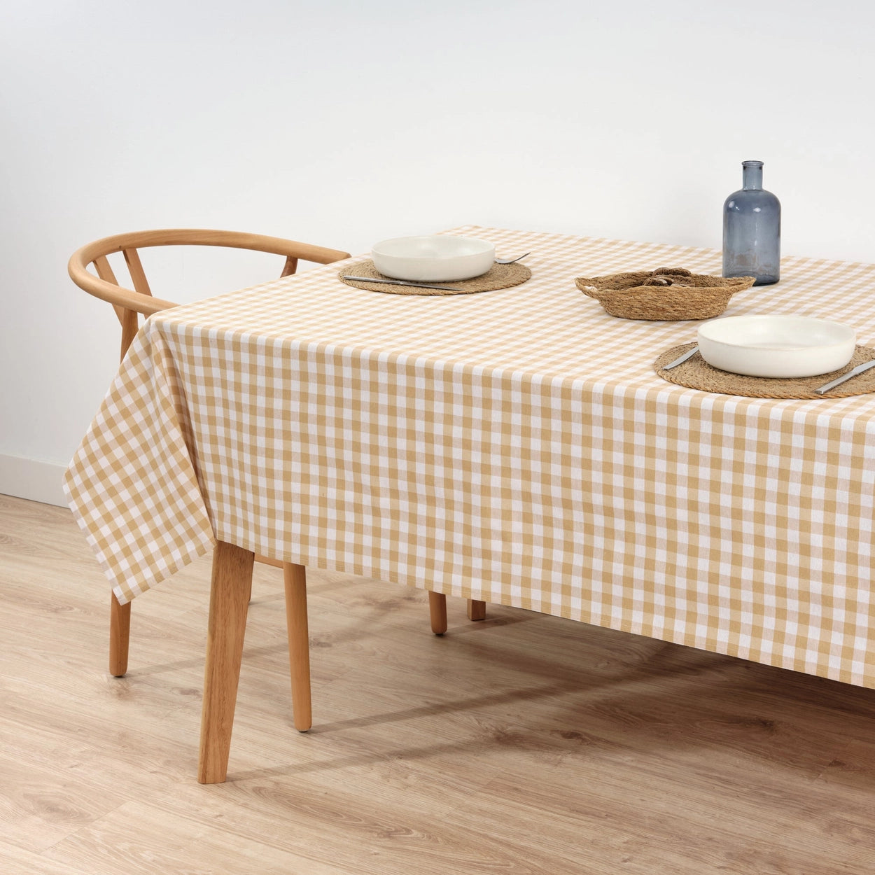 Table with a beige and white checkered tablecloth, wooden chair, and white bowl on a light background