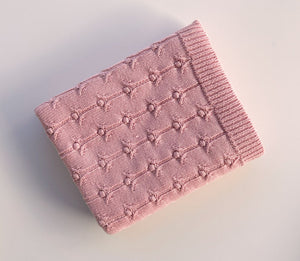Pink knitted blanket with a textured pattern on a light background