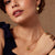 Close-up of a woman wearing gold jewelry including earrings, necklace, and ring on a neutral background