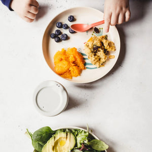 Children's hands reaching for a plate of food on a white surface