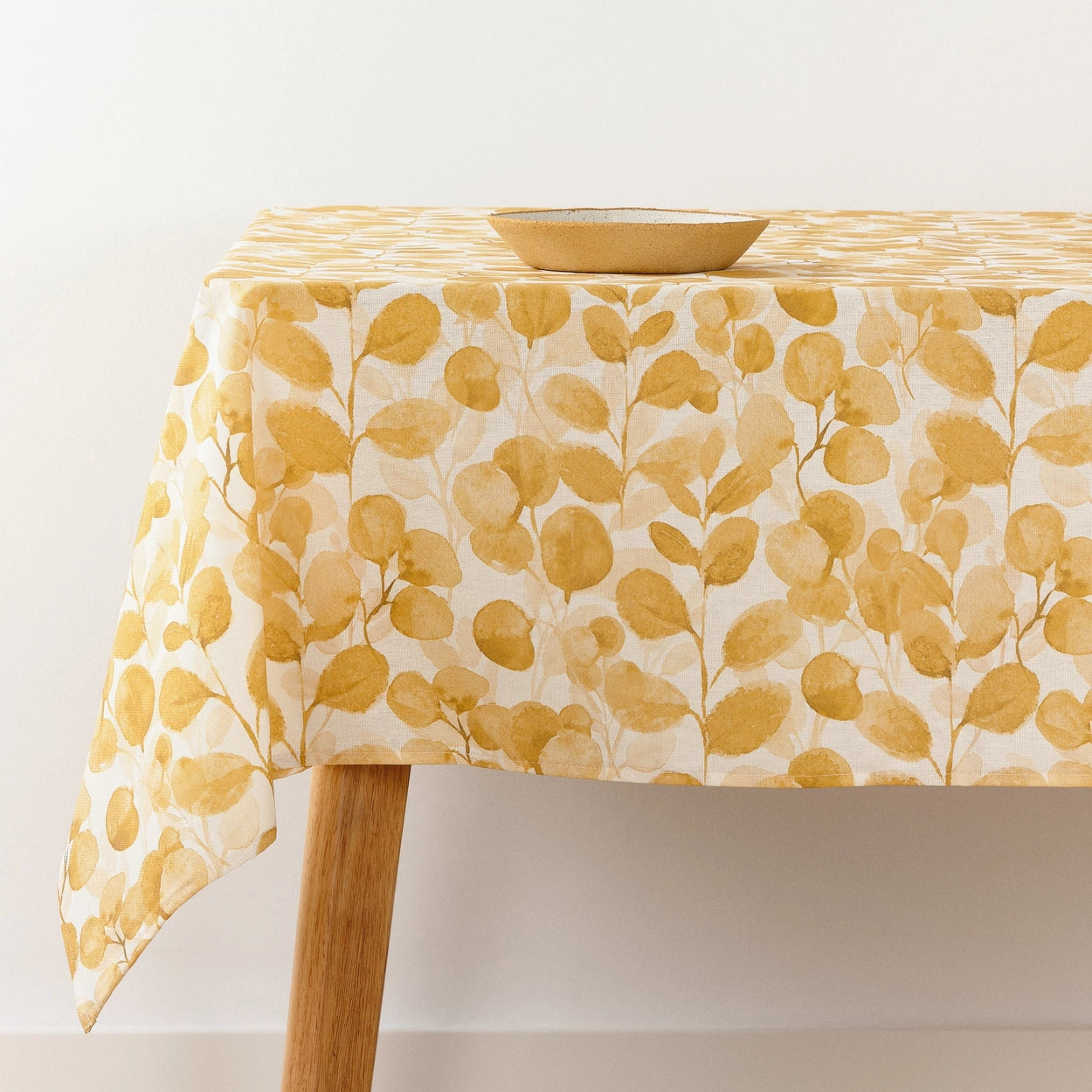 Table with a yellow leaf patterned tablecloth on a white background