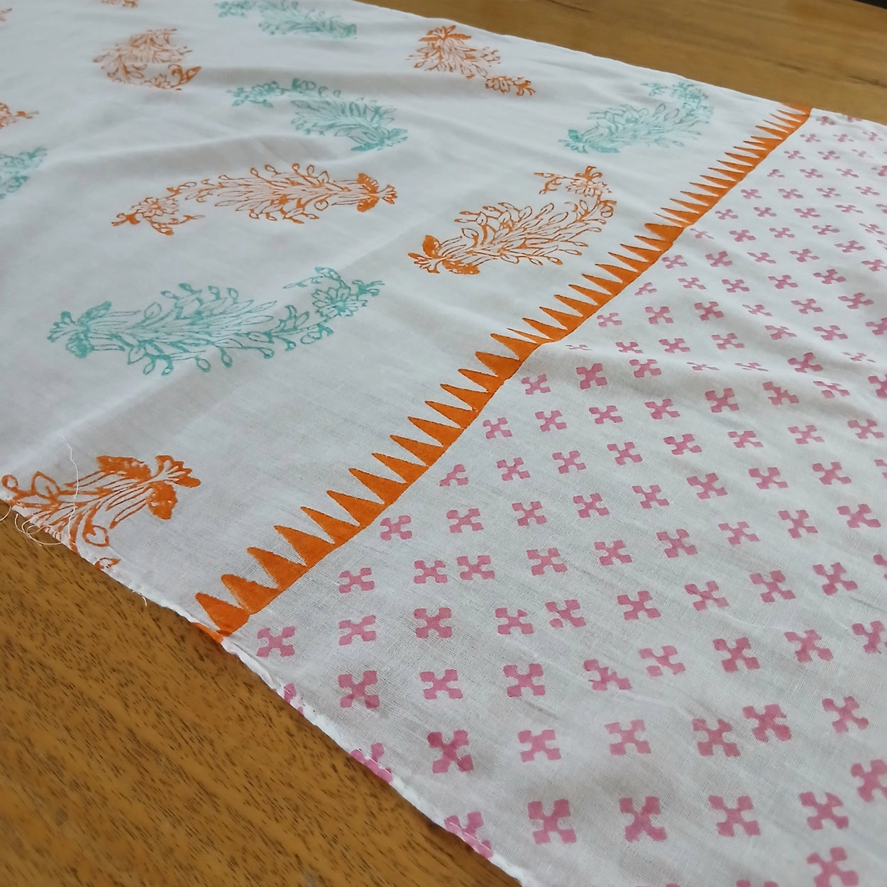 White scarf with pink, orange and green floral patterns draped over a wooden surface