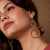 Close-up of a woman wearing gold hoop earrings with a neutral background