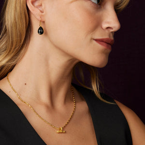 Close-up of a woman wearing gold necklaces and earrings against a dark background