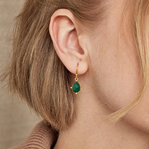 Close-up of a person wearing a gold earring with a green gemstone against a neutral background