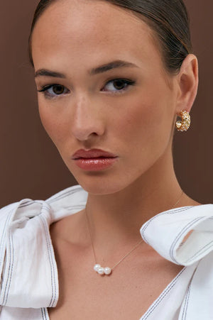 Woman wearing a white blouse with a pearl necklace and earrings against a brown background