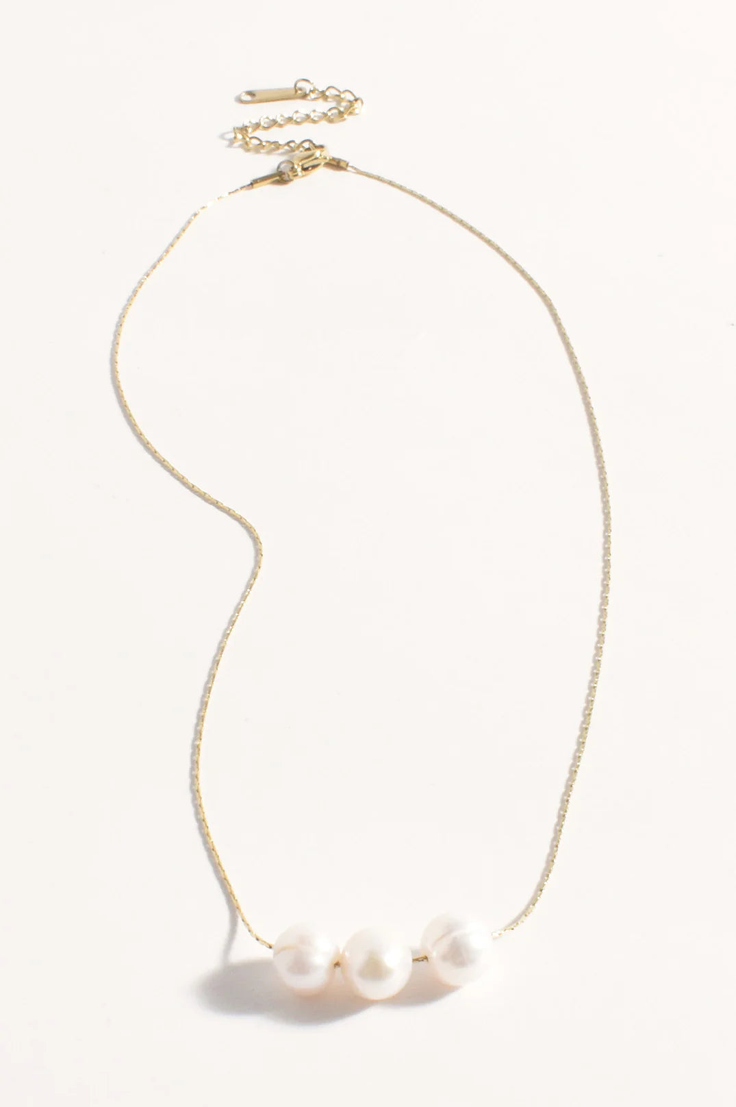 Gold necklace with three pearls on a white background