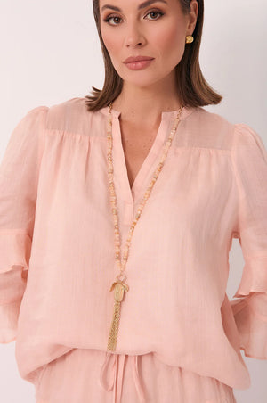 Woman wearing a pink blouse with a long necklace against a white background