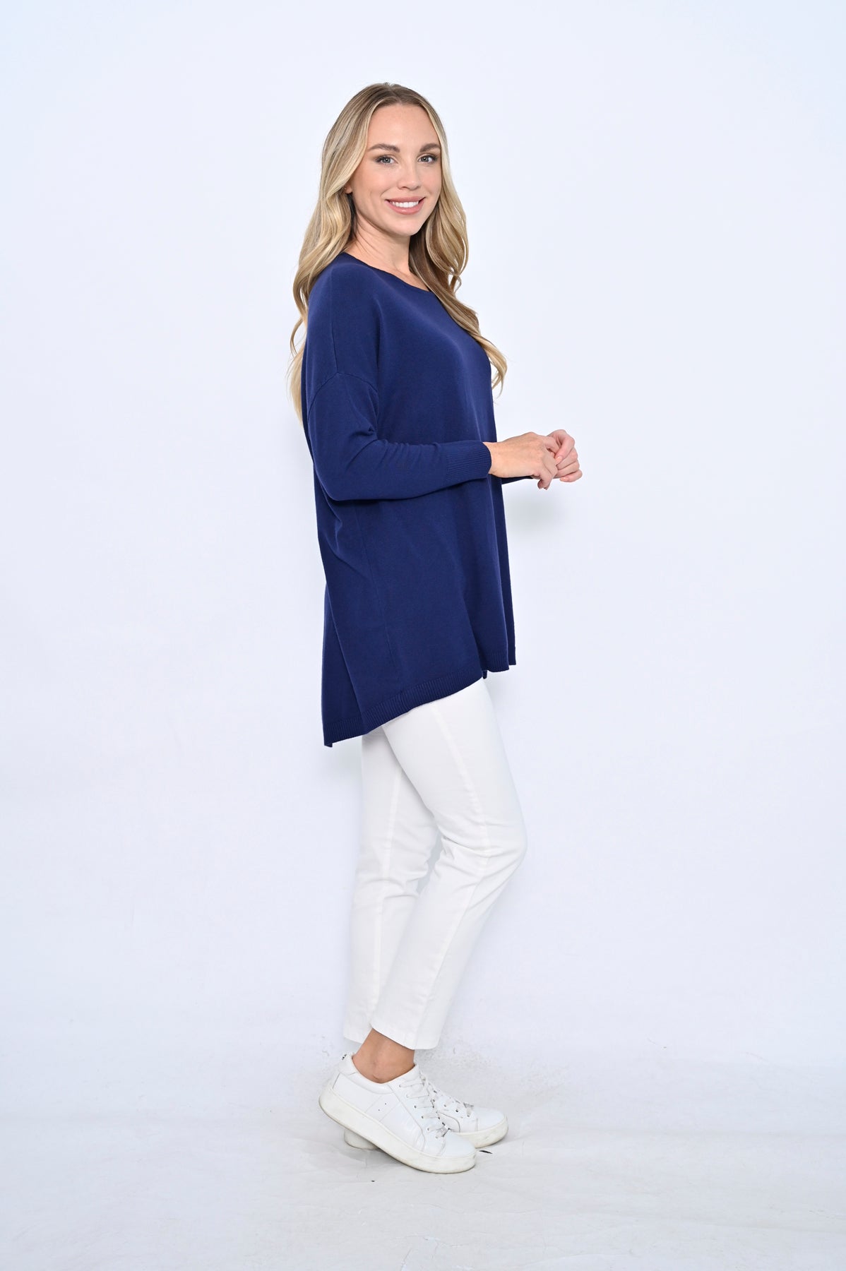 Woman wearing a navy blue sweater and white pants on a white background
