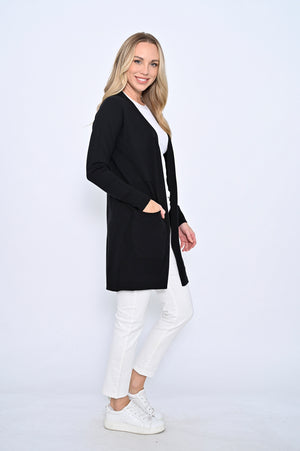 Woman wearing a black cardigan over a white top and pants on a white background