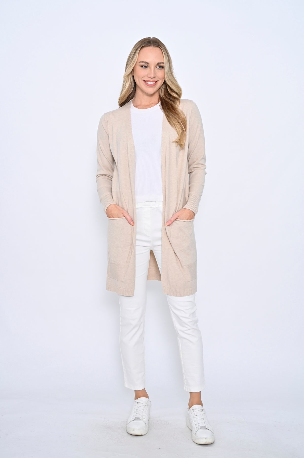 Woman wearing a beige cardigan over a white top and pants on a white background