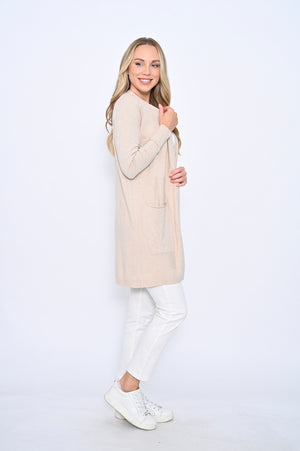 Woman wearing a beige long sweater over a white top and pants on a white background