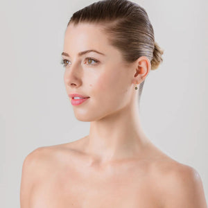 Woman  against a plain background with huggie drop earrings