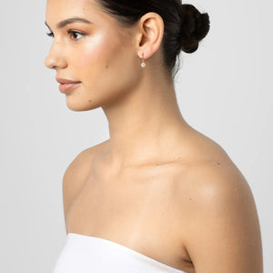 Woman with a stylish hair bun wearing a white strapless top against a plain background