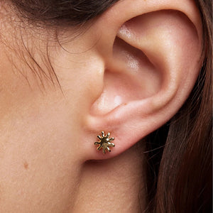 Close-up of an ear wearing a gold earring with a sunflower design.