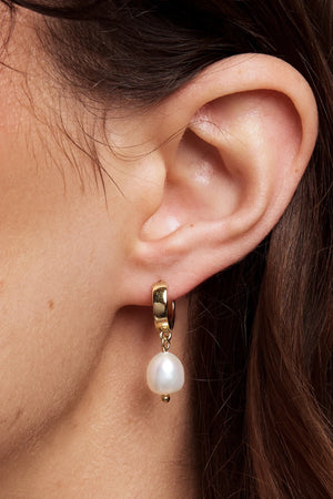 Close-up of an ear wearing a gold hoop earring with a pearl drop.