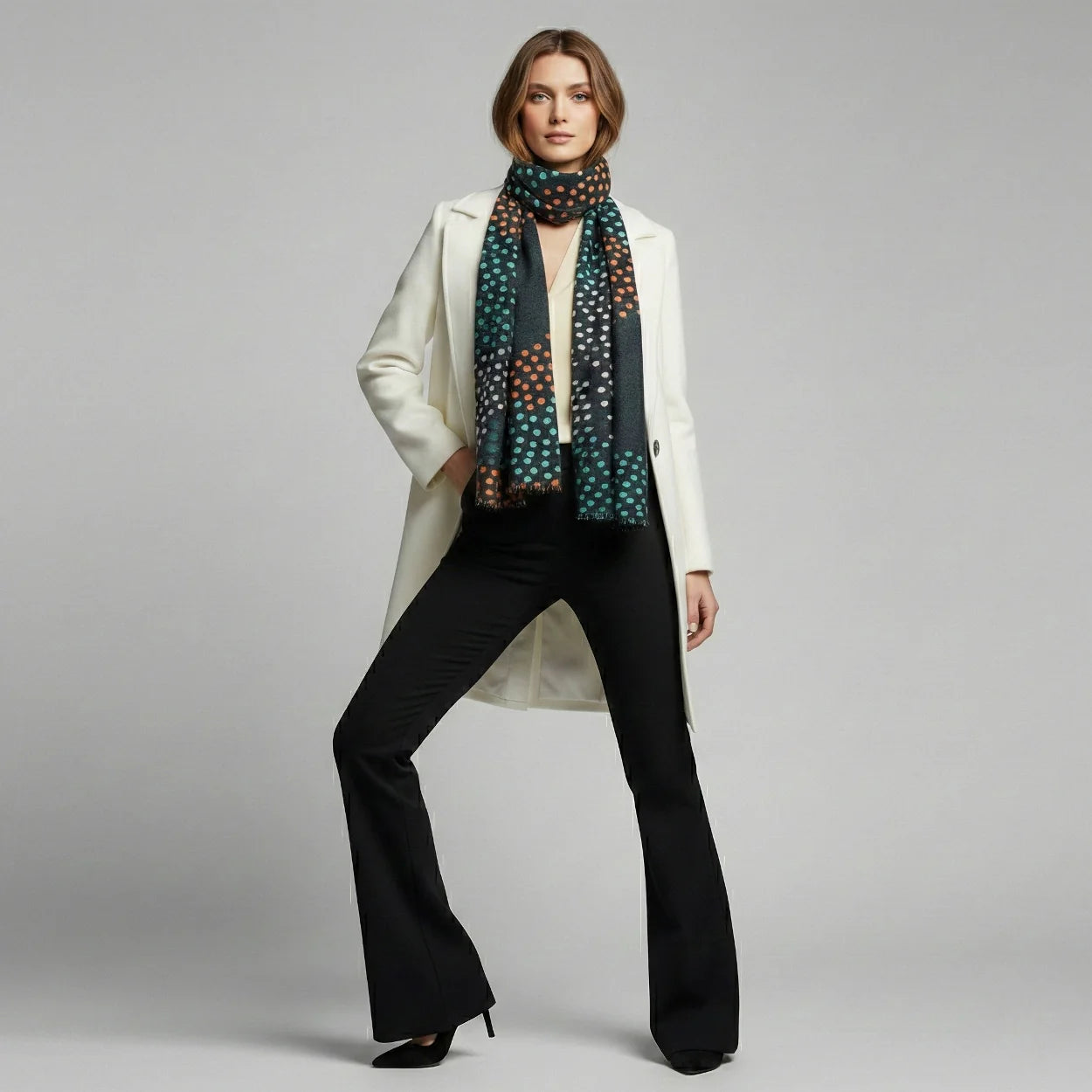 Woman wearing a white coat, black pants, and a patterned scarf on a gray background