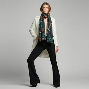 Woman wearing a white coat, black pants, and a patterned scarf on a gray background