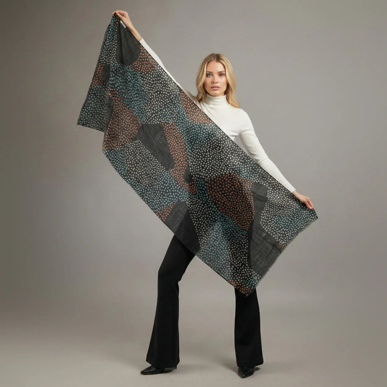 Woman wearing a white coat, black pants, and a patterned scarf on a gray background