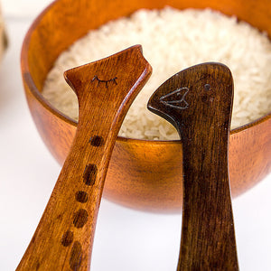 Two Wooden spoons with engraved faces in a wooden bowl filled with rice.