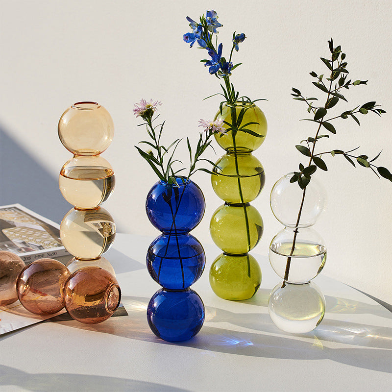 Colorful glass vases with stems on a light surface