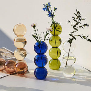 Colorful glass vases with stems on a light surface