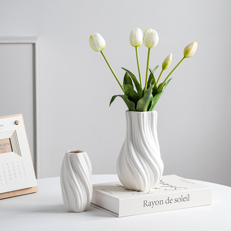 White textured vase with tulips on a book against a light gray background