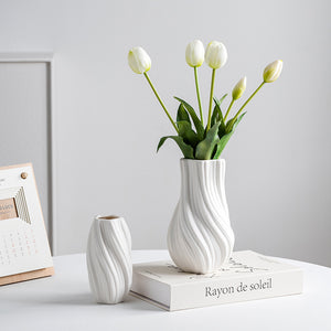 White textured vase with tulips on a book against a light gray background