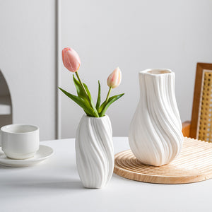 Two white ceramic vases with a small bouquet of pink tulips on a light surface.