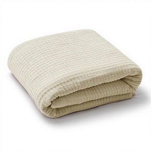 A folded cream-colored cotton muslin blanket with a textured waffle pattern, shown on a clean white background.
