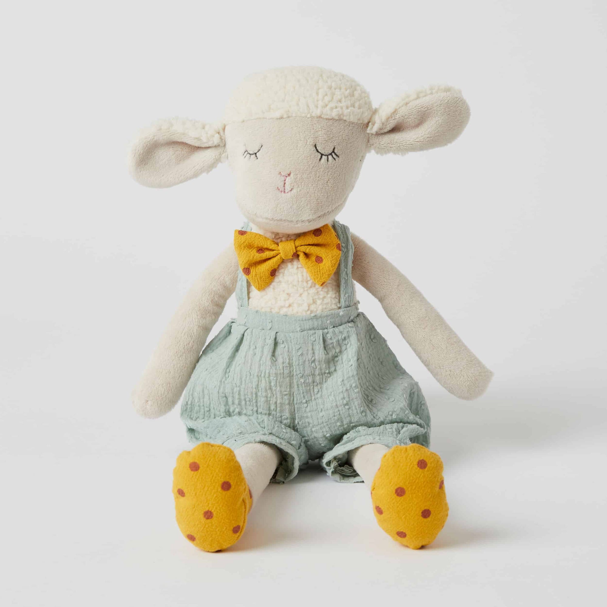 Stuffed toy sheep with a yellow bow tie and green overalls on a white background