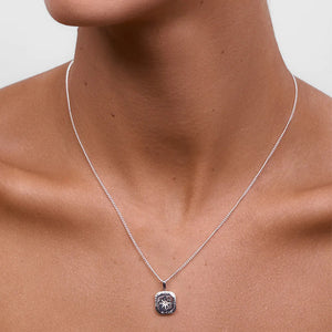 Silver necklace with a pendant on a person's neck against a neutral background
