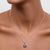 Silver necklace with a pendant on a person's neck against a neutral background