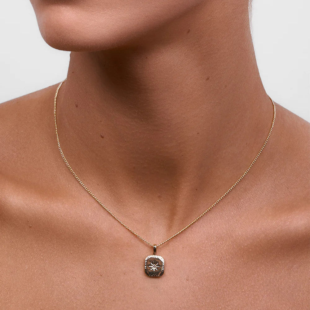 Gold necklace with a pendant on a person's neck against a neutral background