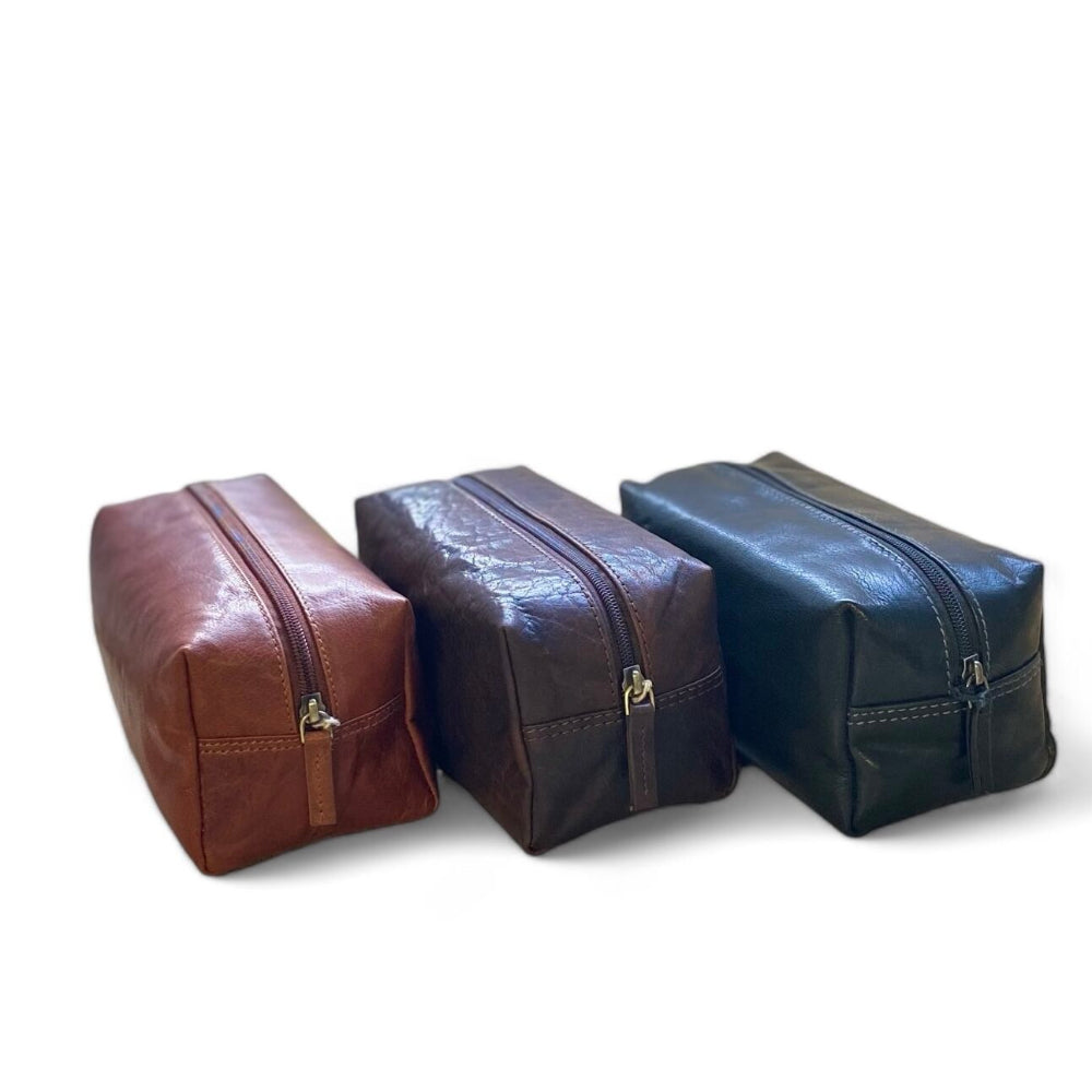 Three leather toiletry bags in brown, black, and cognac on a white background