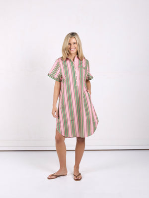 A woman modeling a short-sleeve button-front shirt dress with vertical pink, green, and white stripes, standing against a plain white studio background.
