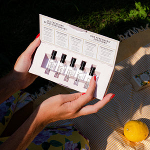Person holding a small box with miniature perfume bottles and labels outdoors.